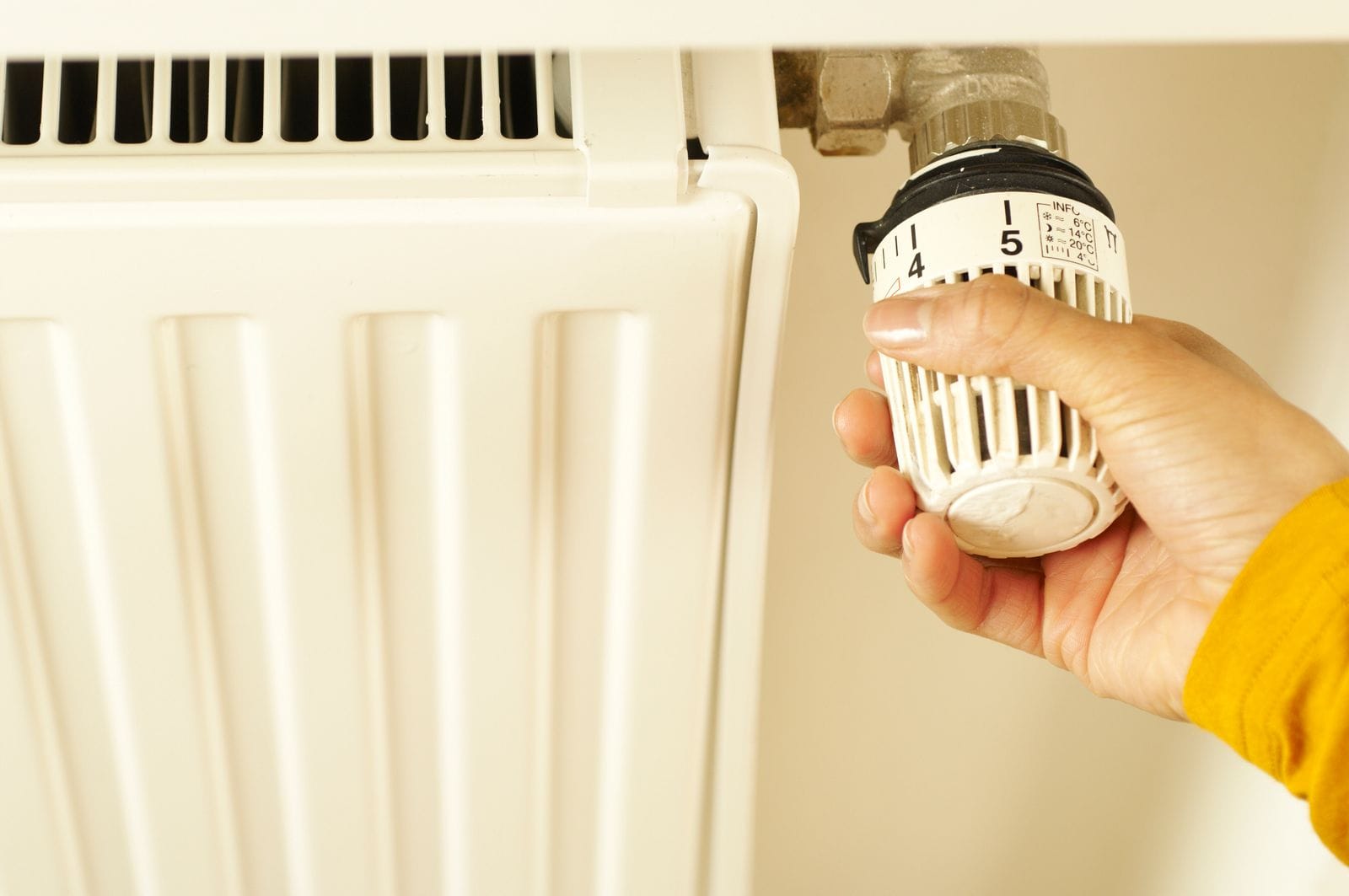 Mano ajustando la válvula termostática de un radiador para regular la temperatura de la vivienda